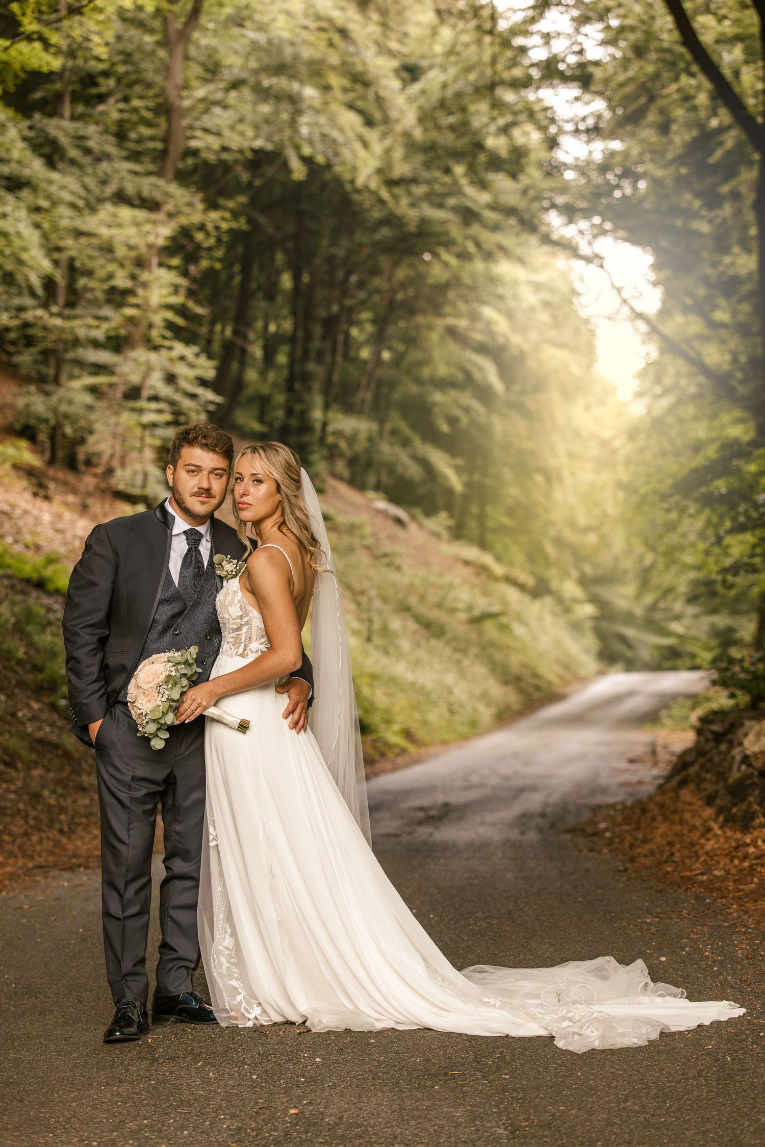 A couple in wedding attire share an intimate moment on a misty forest road during an autumn photo session.