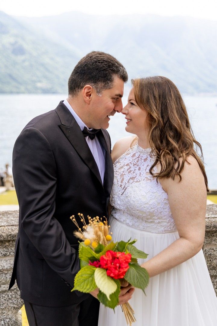 A couple shares an intimate moment on a lakeside terrace with a colorful bouquet.