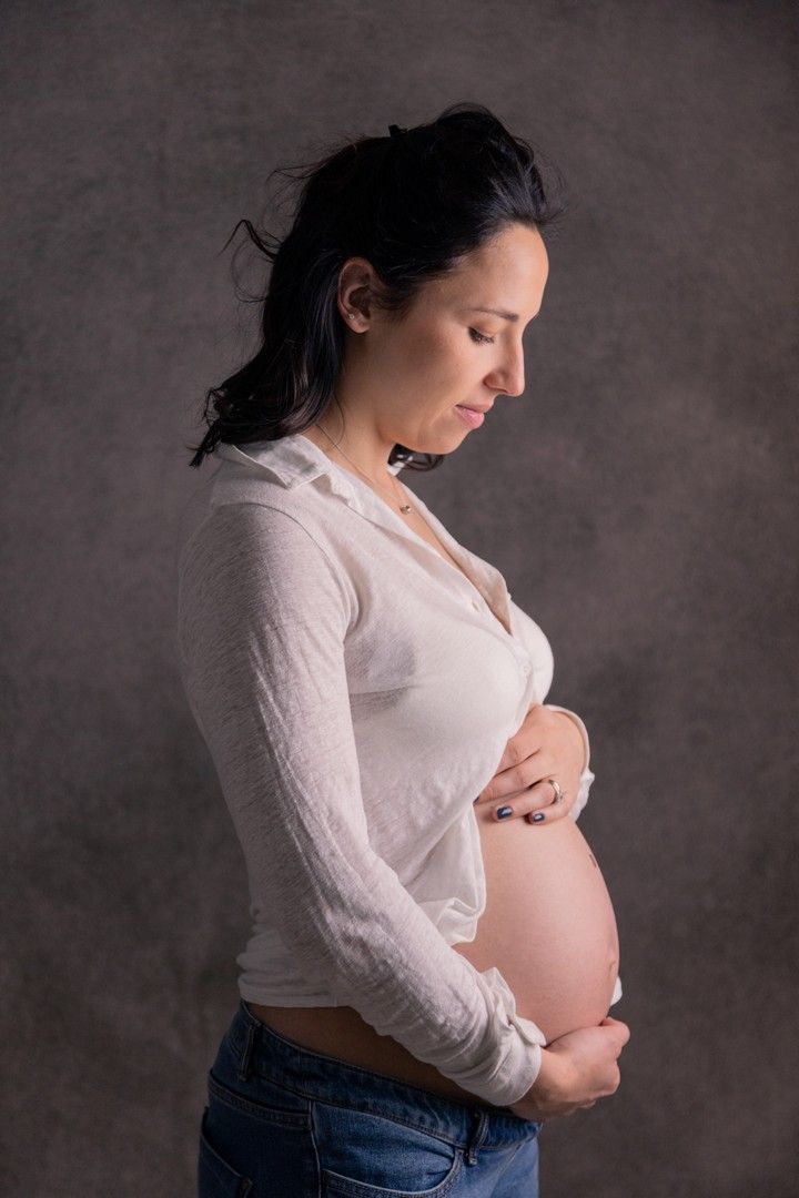 Side profile maternity portrait against dark background showing pregnant belly.