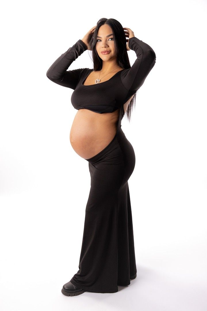 Maternity photo of an expectant mother in a black form-fitting dress posing against white background.