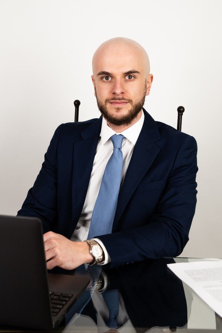 Professional in a navy suit and blue tie seated at a desk in a business setting.