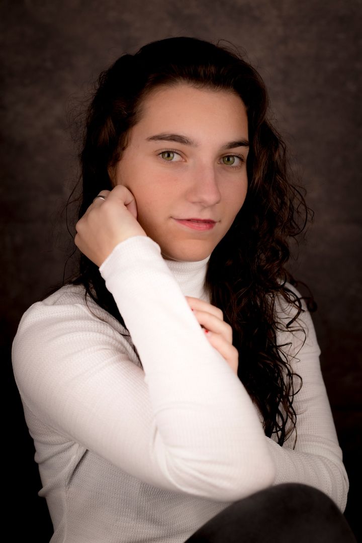 Portrait series in white sweater against dark background with moody lighting.