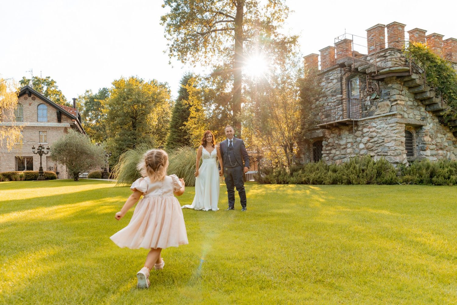 A couple dances playfully in a sunlit garden with historic buildings in the background.