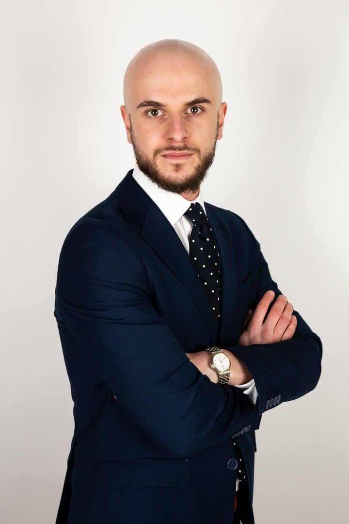Professional in navy suit and polka dot tie posing with crossed arms.