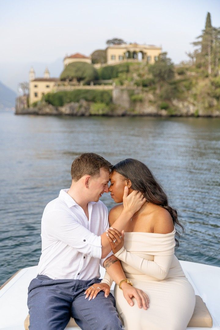 Romantic couple sharing an intimate moment on a boat with a scenic Italian lake villa in the background.