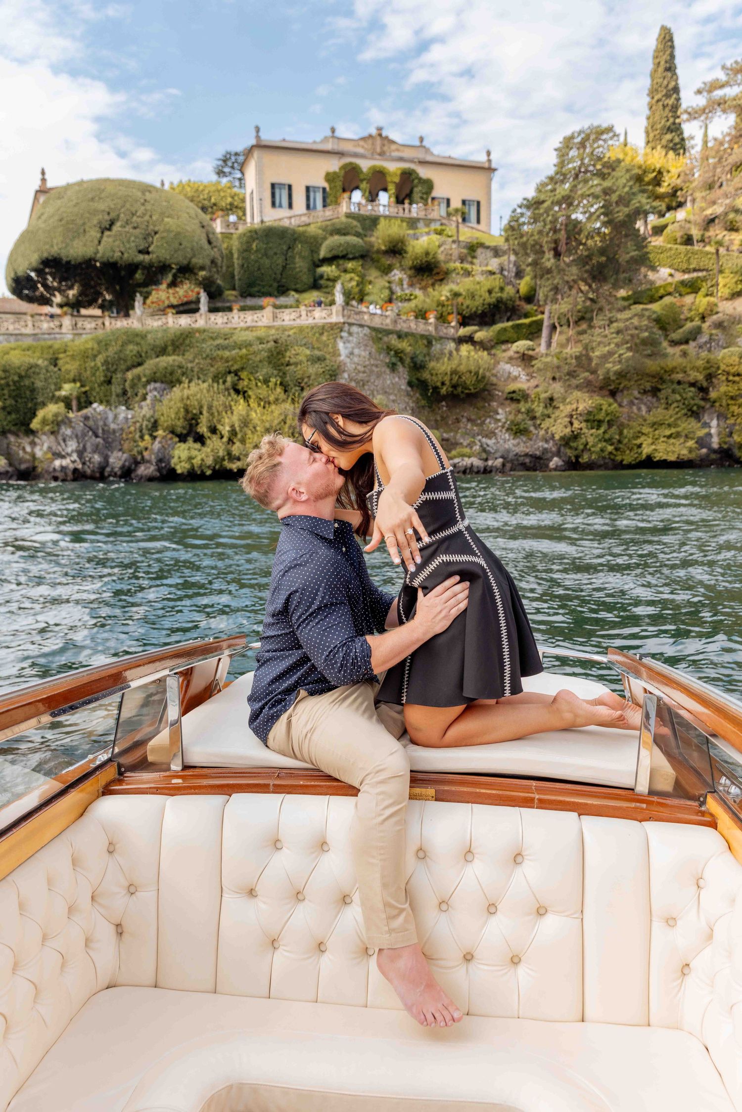 Romantic embrace on classic wooden boat with Italian lakeside architecture.
