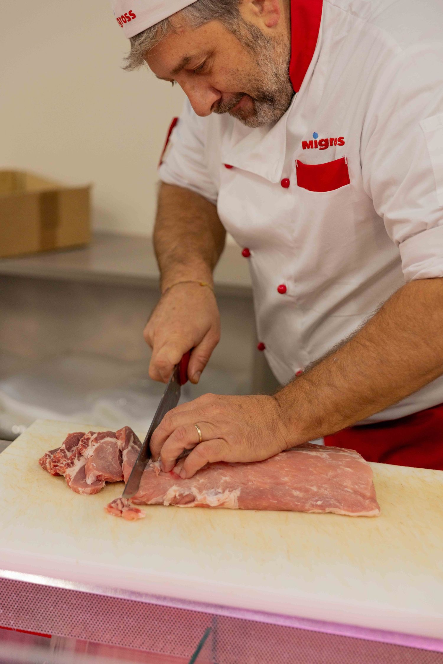 Butcher in white uniform carefully cutting meat on cutting board.