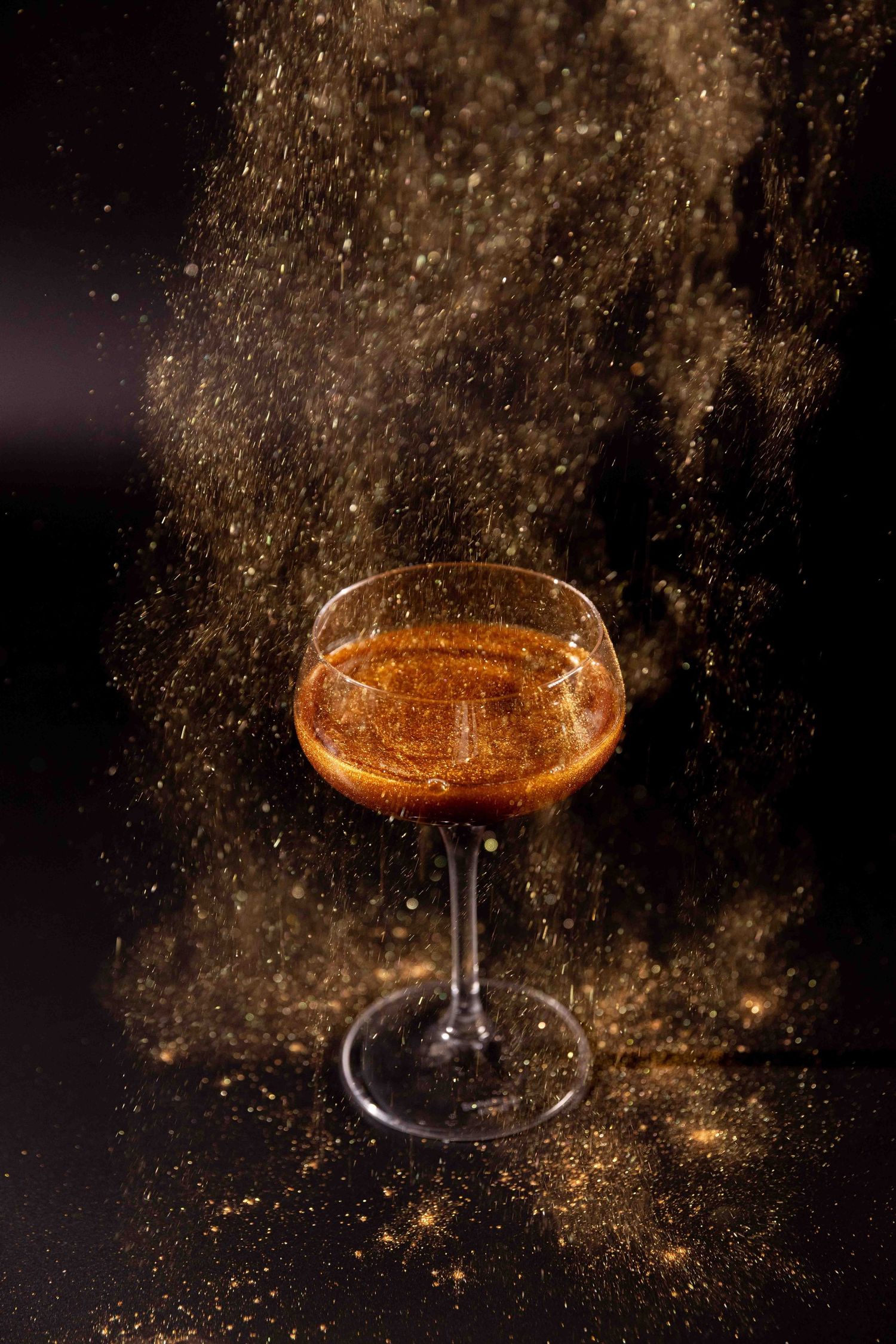 Sparkling cocktail glass captured with glittering golden bokeh effect against dark background.