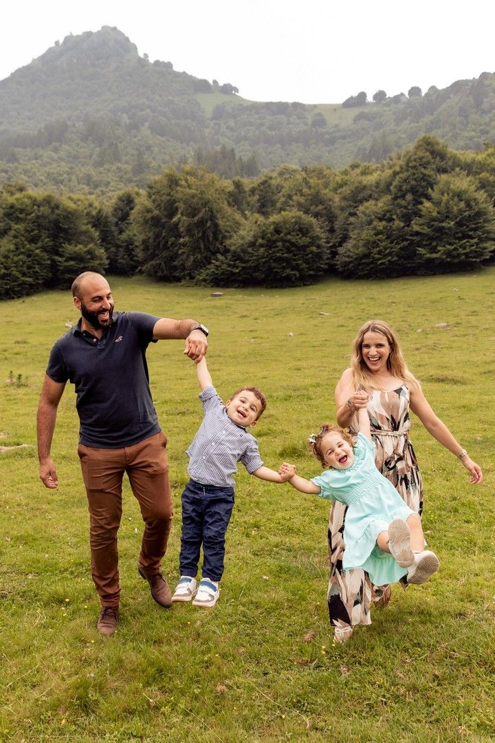 Family playing and swinging children in grassy mountain meadow.