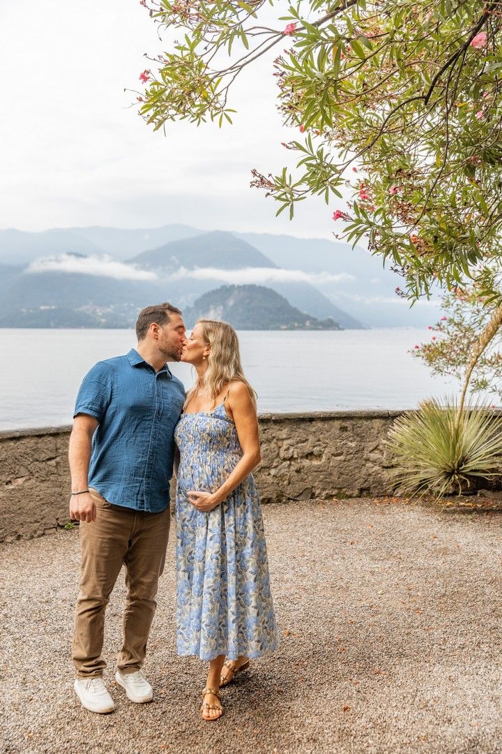 Couple shares tender moment on lakeside path with mountain backdrop.