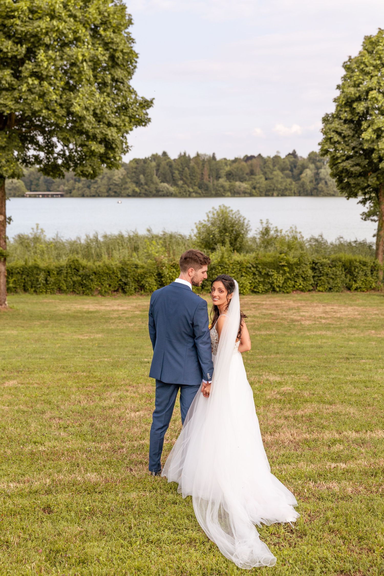 Newlyweds share an intimate moment in a sunlit meadow with flowing white dress and navy suit.