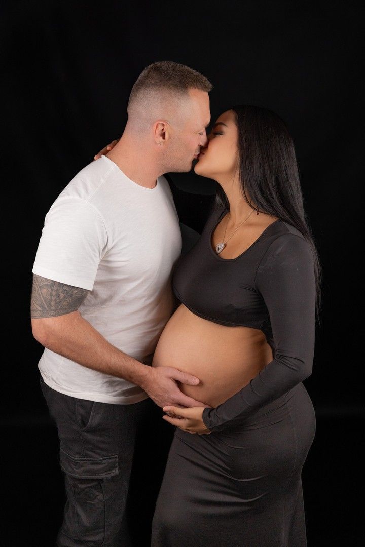 Intimate maternity portrait against dark background with dramatic lighting.
