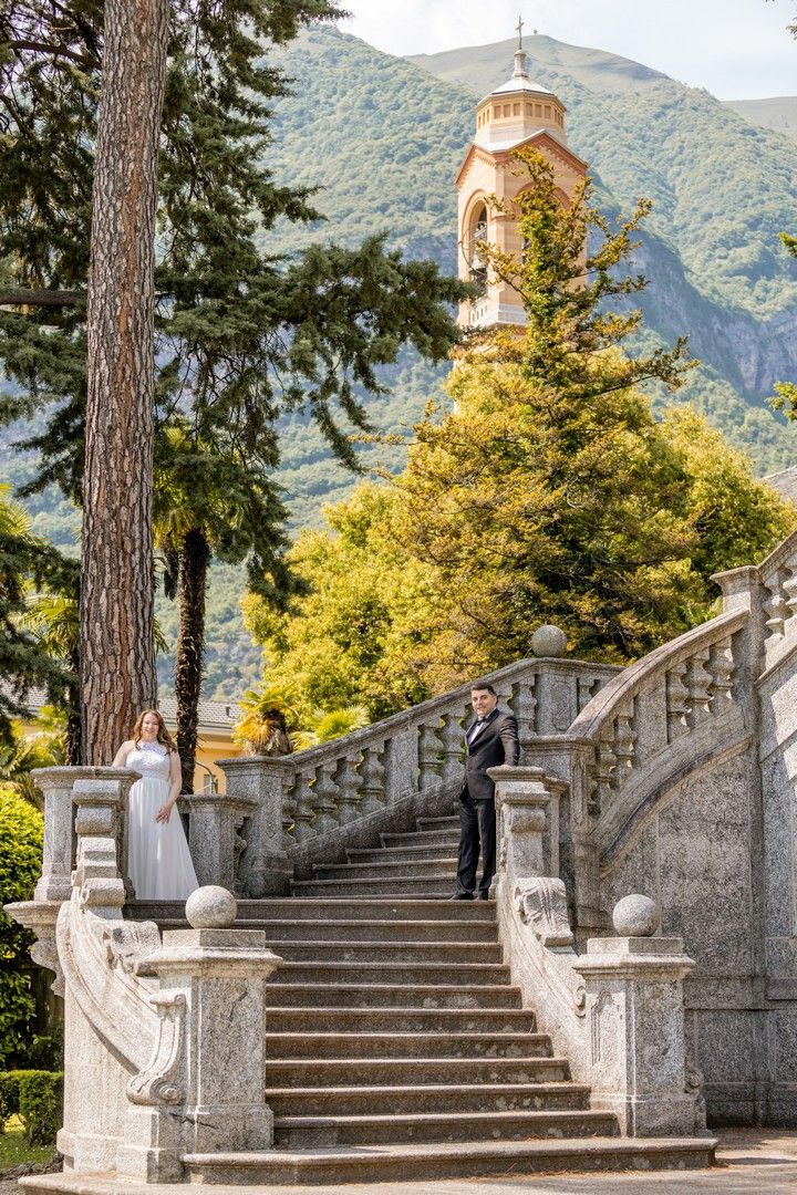 Grand stone staircase with ornate balusters leading up to a bell tower with mountain backdrop.