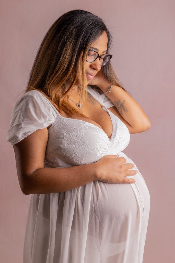 Woman in white lace dress cradles her baby bump in studio portraits.