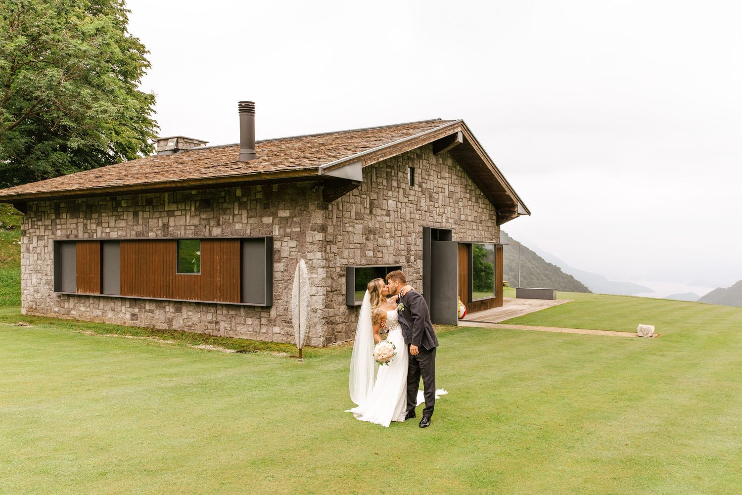 Modern stone and wood building nestled in a lush green landscape.