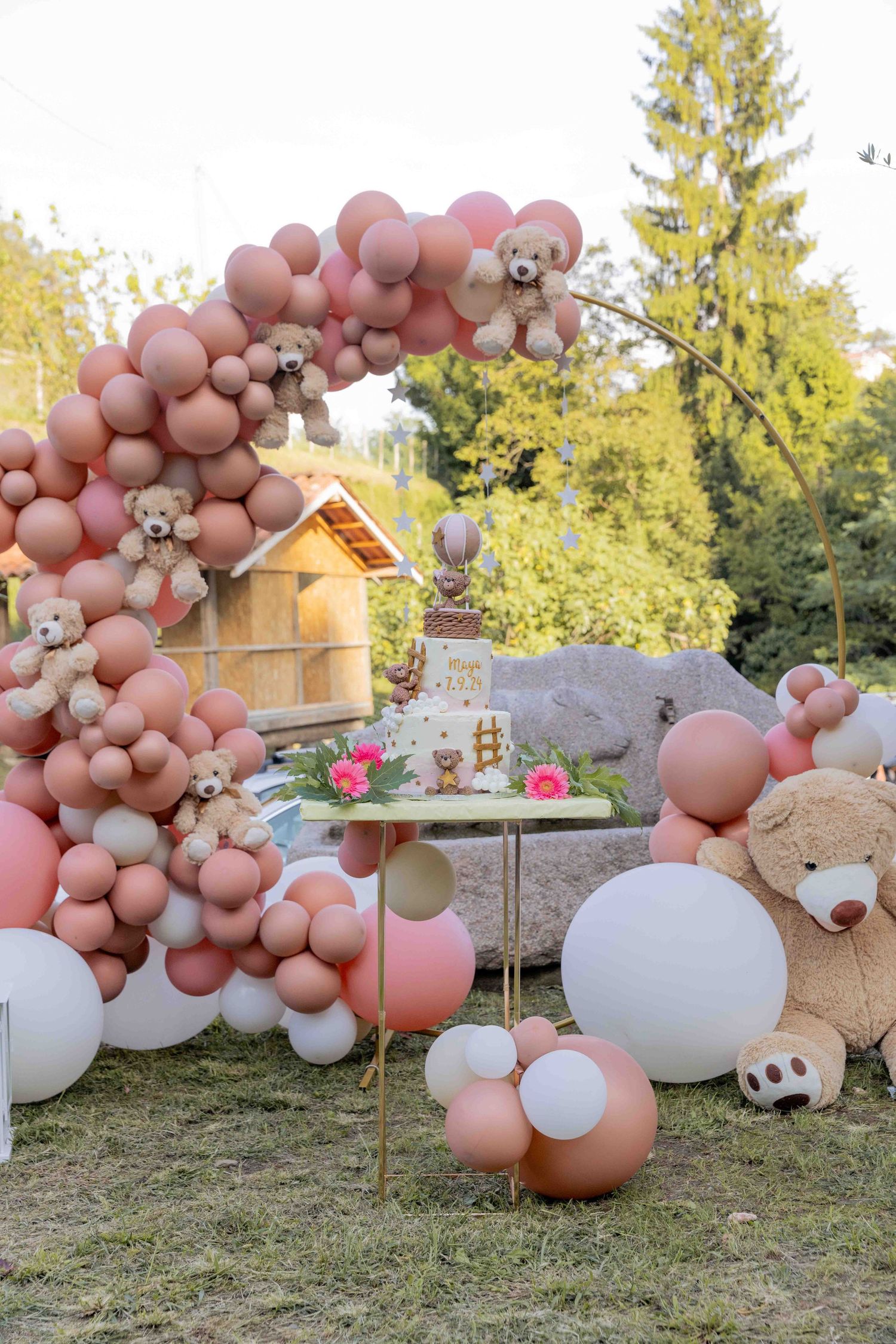 Pink and white balloon arch with teddy bears creates a whimsical outdoor party decoration.