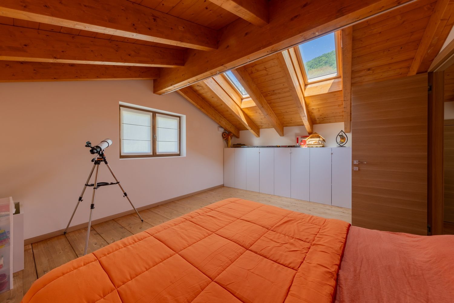 Spacious attic room with wooden ceiling beams and terracotta flooring.