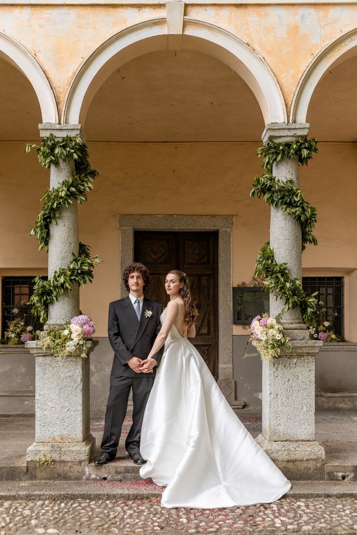 A couple poses under elegant stone archways decorated with greenery and flowers.
