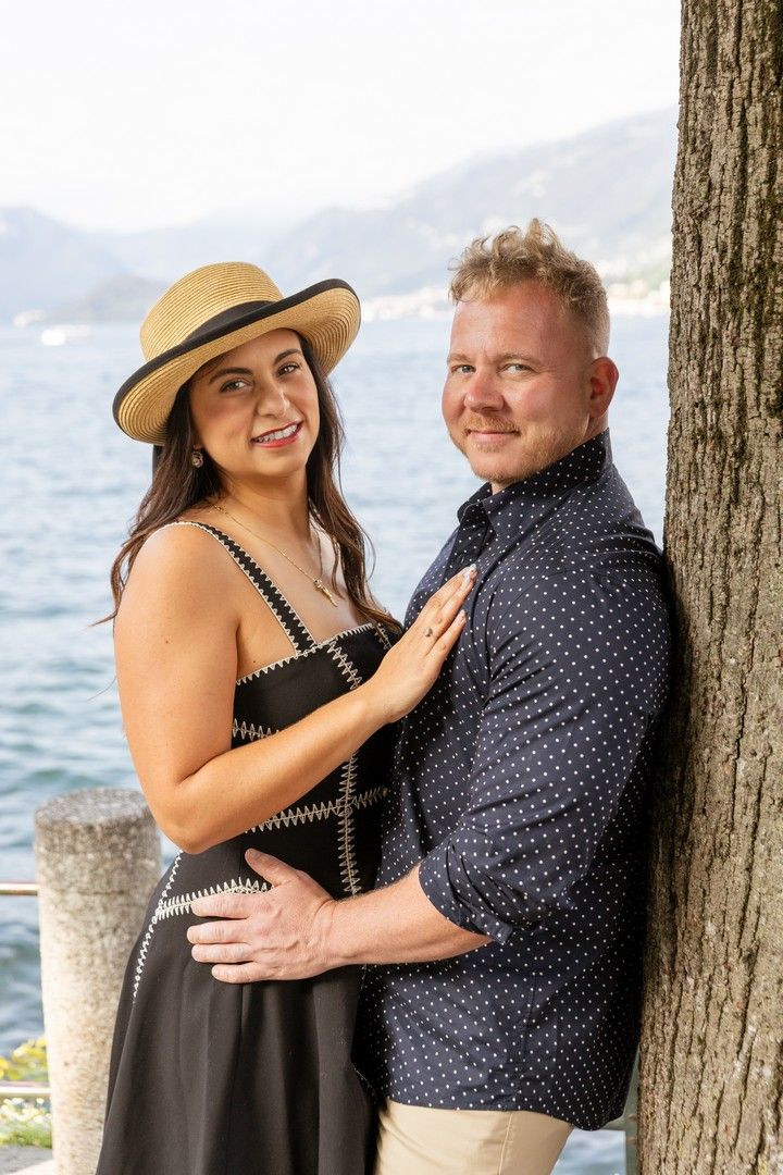 Romantic couple posing by wooden posts near a lake with mountains in the background.