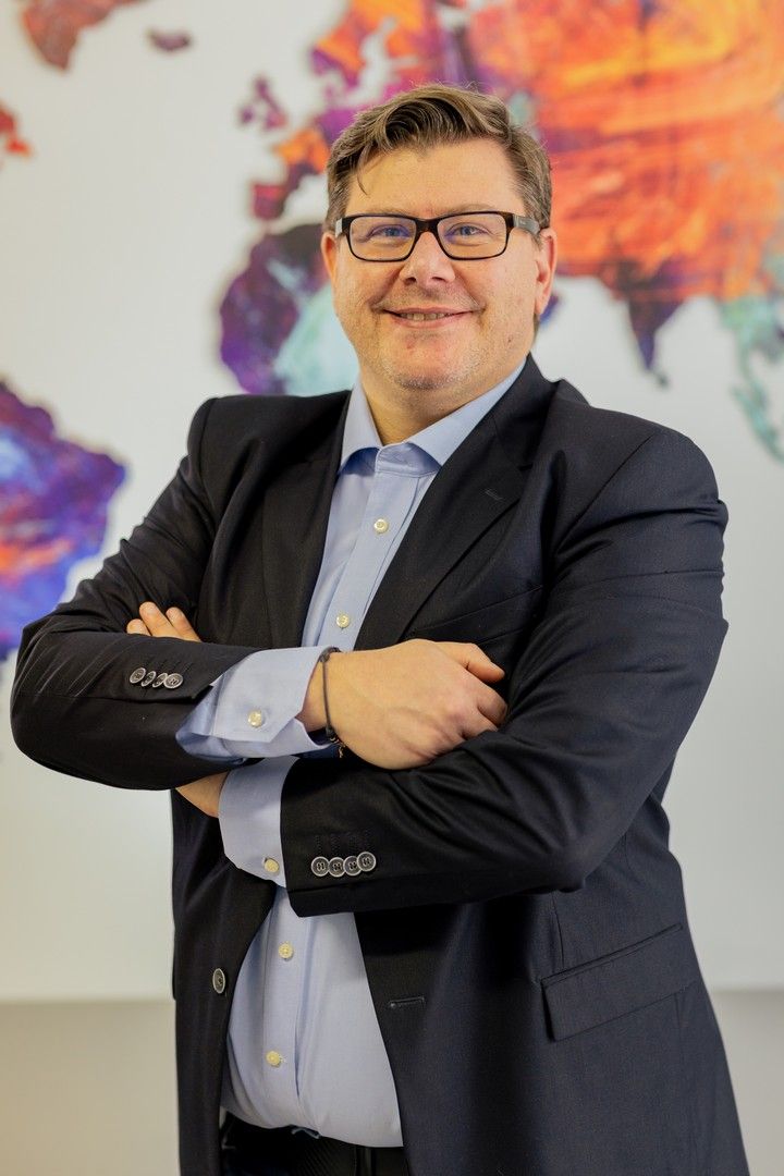 Business professional in a dark suit posing against a vibrant abstract art wall.