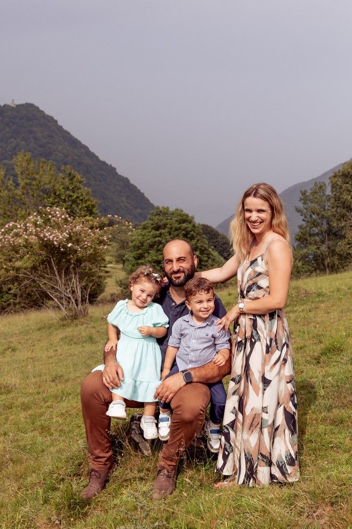Family sitting together on grassy hillside with mountain backdrop.
