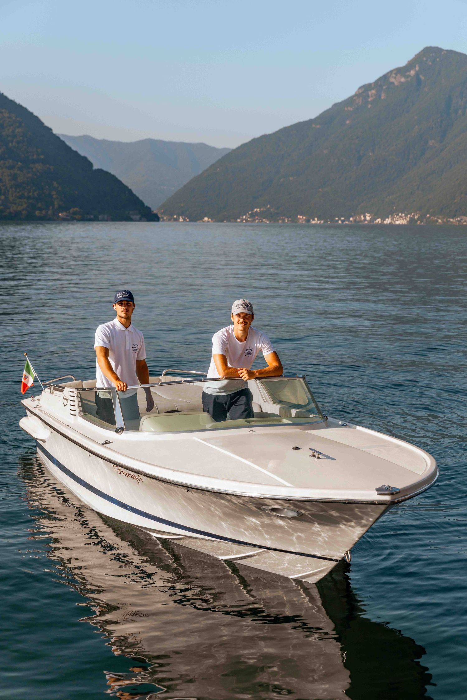 White speedboat glides across calm blue waters with mountain backdrop.