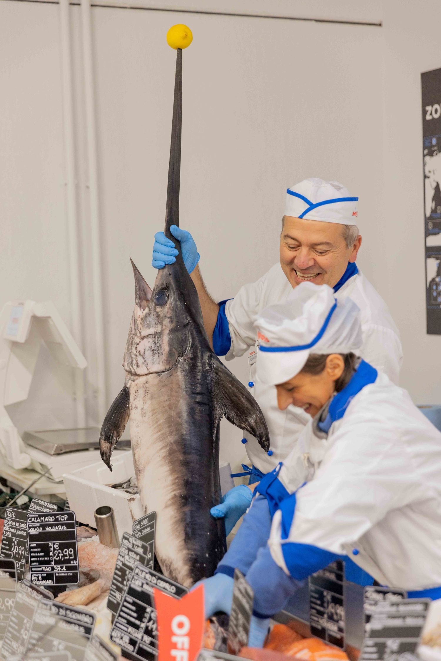 Workers in protective gear handling large fish at seafood counter.