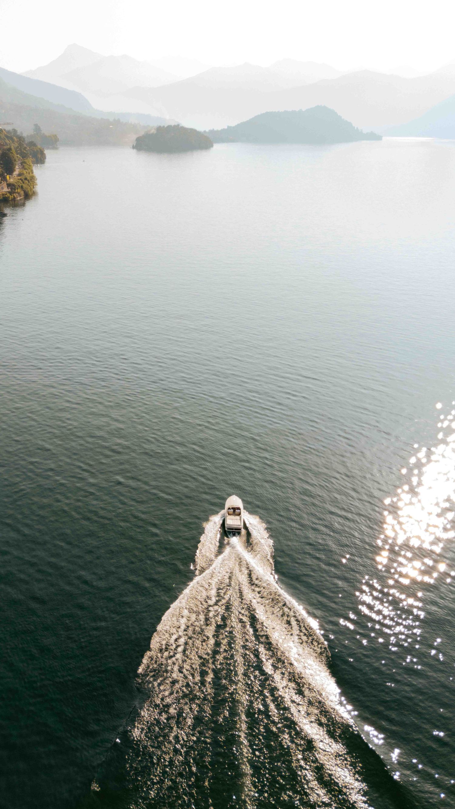 Aerial view of a speedboat creating a wake pattern on a misty mountain lake surrounded by forested shores.