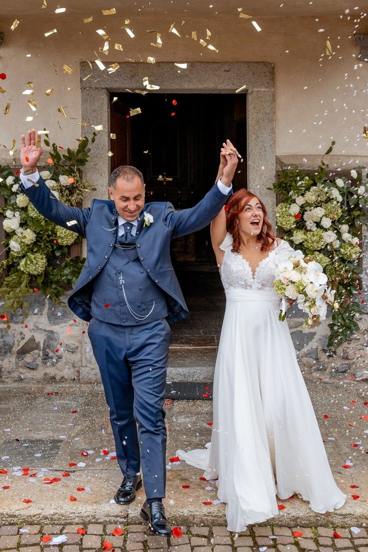 Joyful newlyweds celebrate with confetti being thrown at a rustic stone venue entrance.