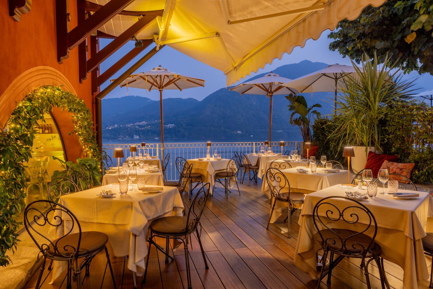Waterfront dining area with outdoor seating, umbrellas, and stunning lake and mountain panorama.