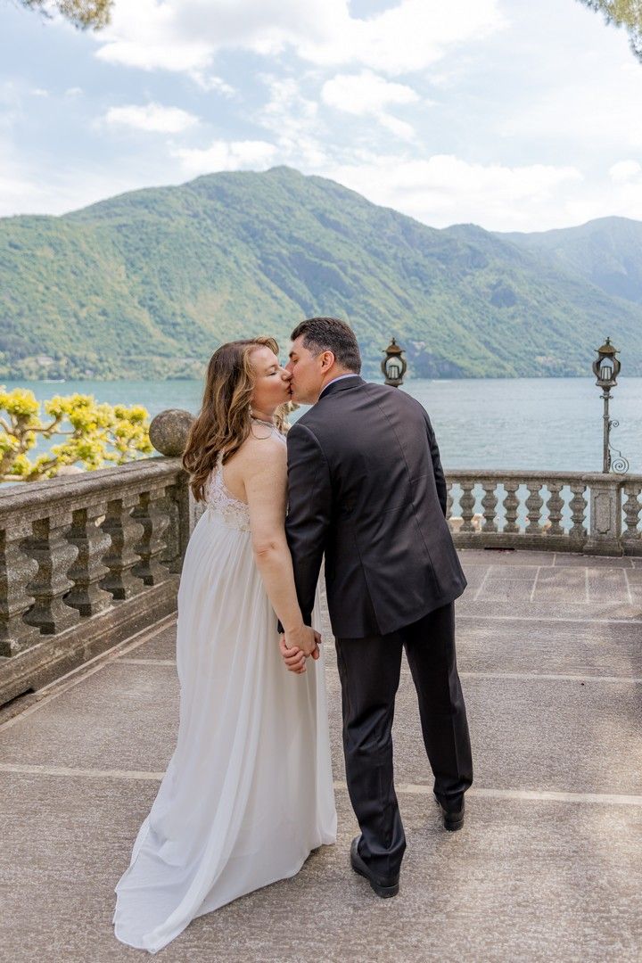 A romantic moment captured on a stone terrace with mountain lake views and ornate railings.