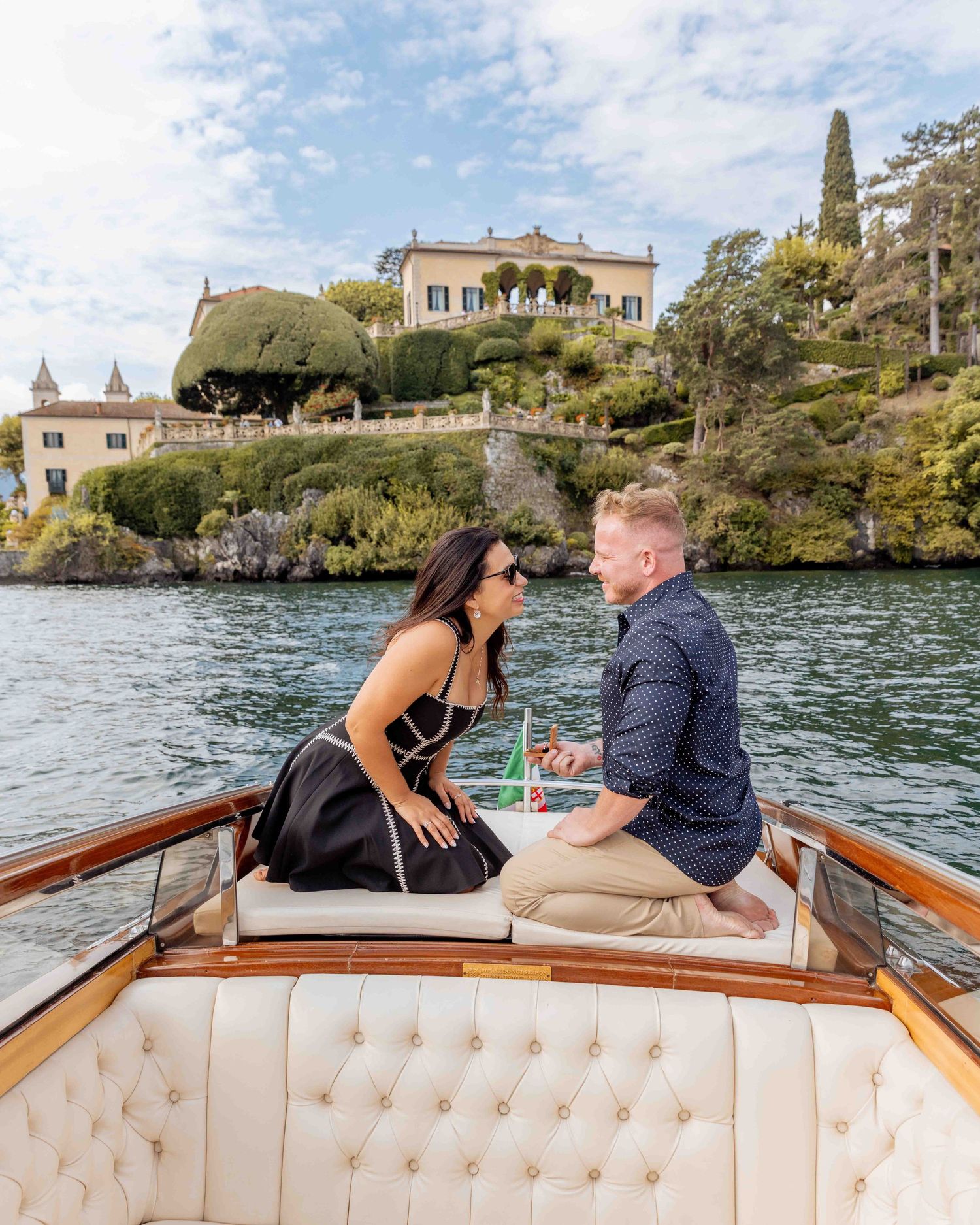 Couple enjoying a romantic boat ride along the coastline with elegant villas and Mediterranean architecture in view.