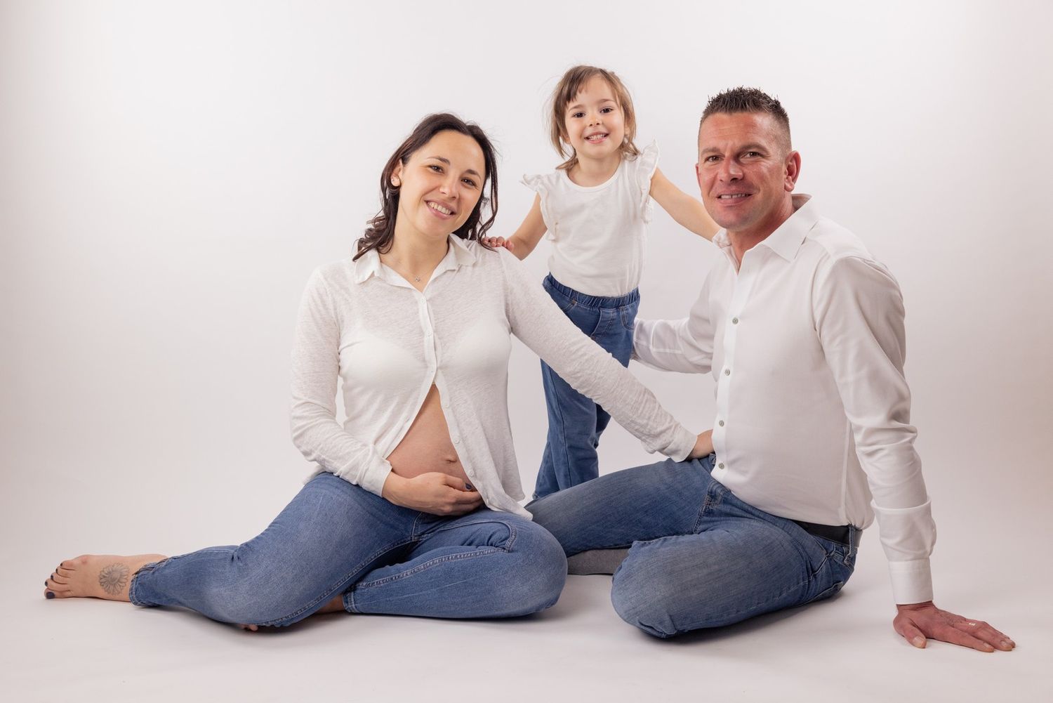 Family maternity photo with young child on white background.