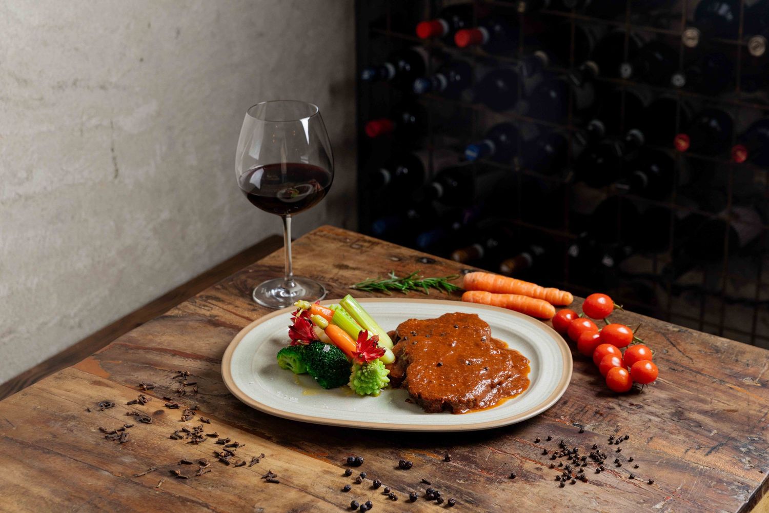 Plated dinner with vegetables and meat on rustic wooden table in dark setting.