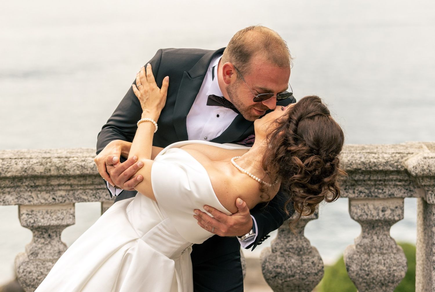 Dramatic wedding dip pose on stone terrace overlooking mountains.