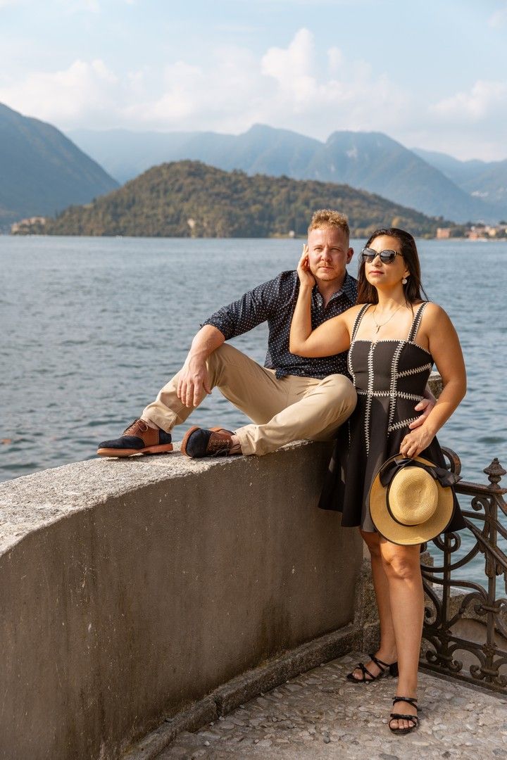 Couple relaxing on stone wall overlooking beautiful mountain lake on sunny day.
