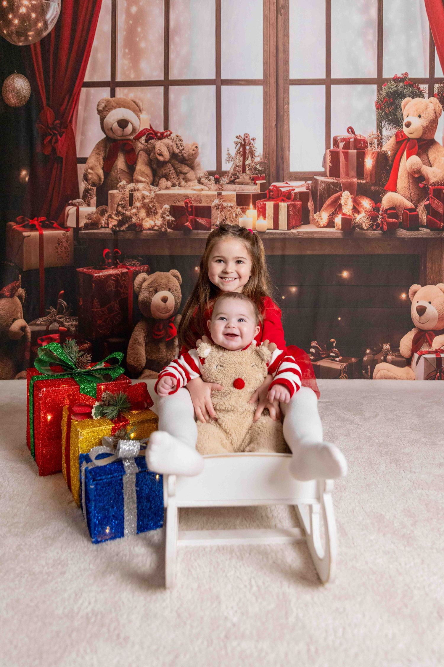 Festive holiday setting with teddy bears, wrapped presents and red curtains.
