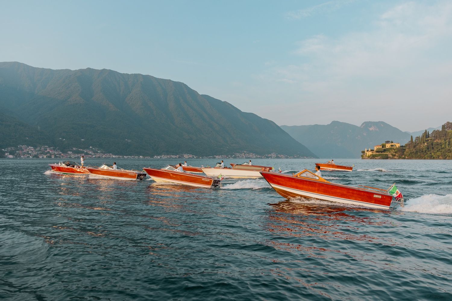 Orange speedboats racing across a scenic mountain lake.