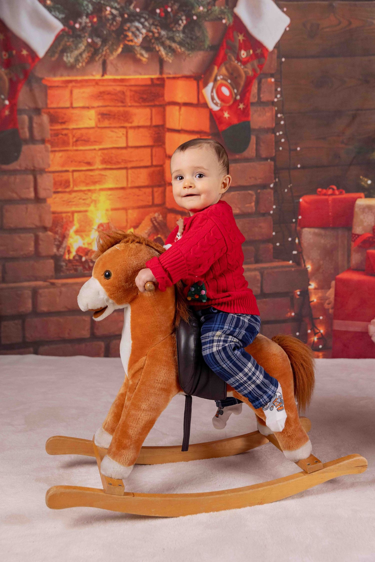 Festive holiday scene with a rocking horse toy against a brick wall with Christmas decorations and twinkling lights.