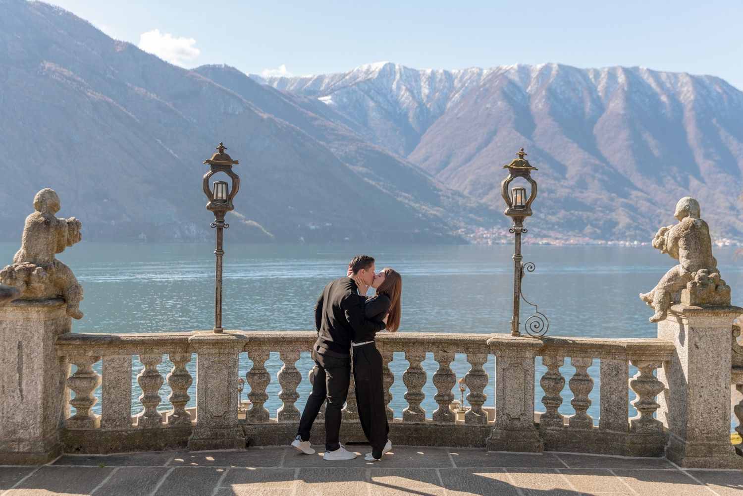 Couple kissing on ornate terrace with lake and mountain views at Lake Como, Italy.