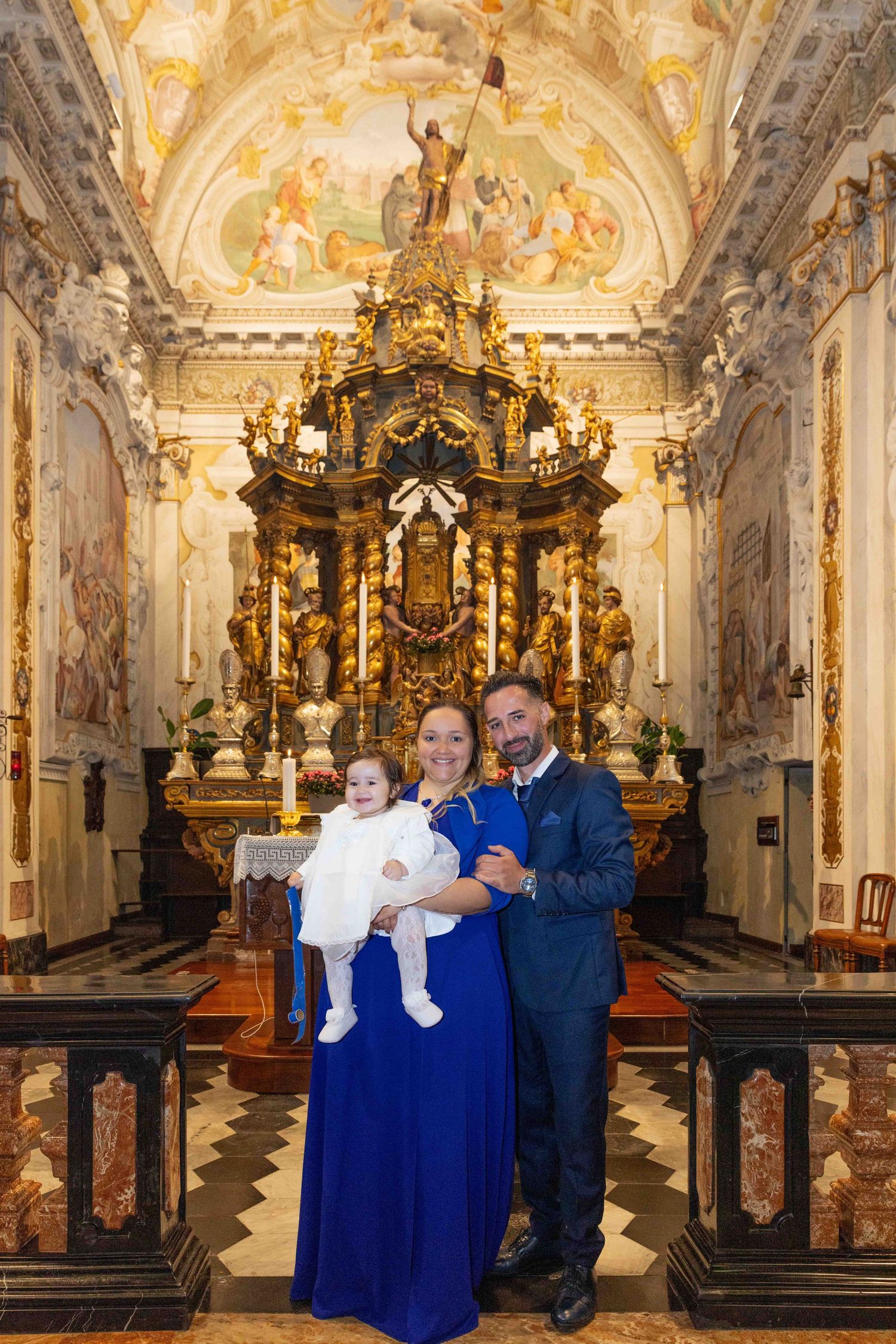 Family portrait in ornate baroque church with gilded altar and painted ceiling.