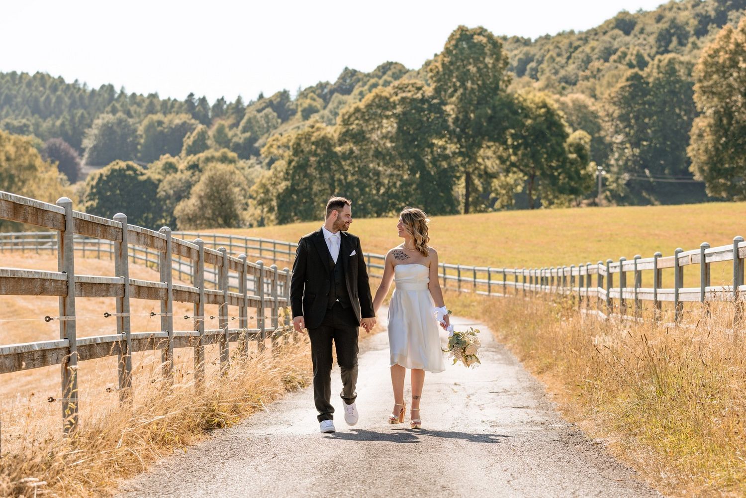 A couple walks along a rustic wooden fence path through golden summer fields.