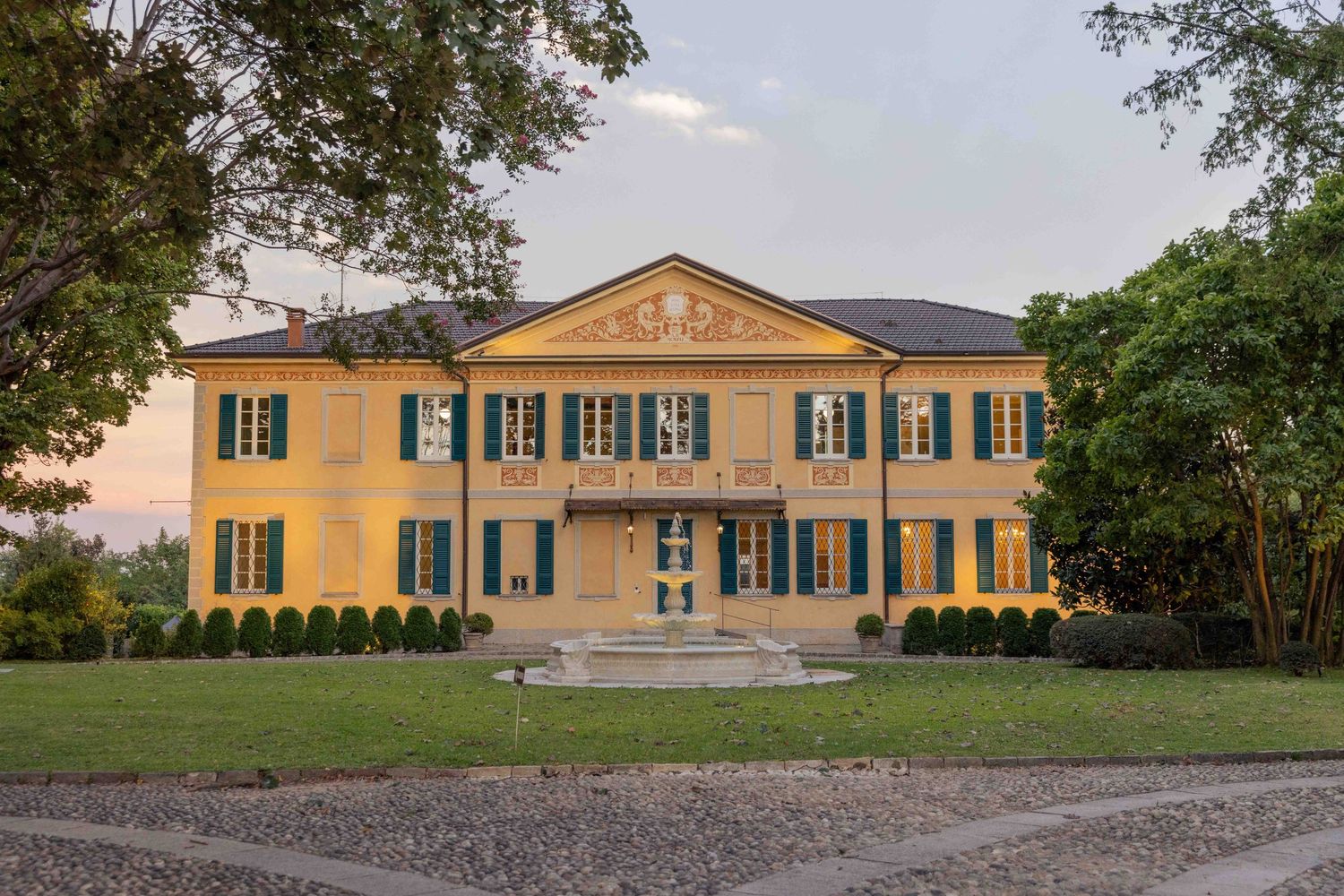 Grand yellow mansion with green shutters and classical architecture set among manicured gardens.