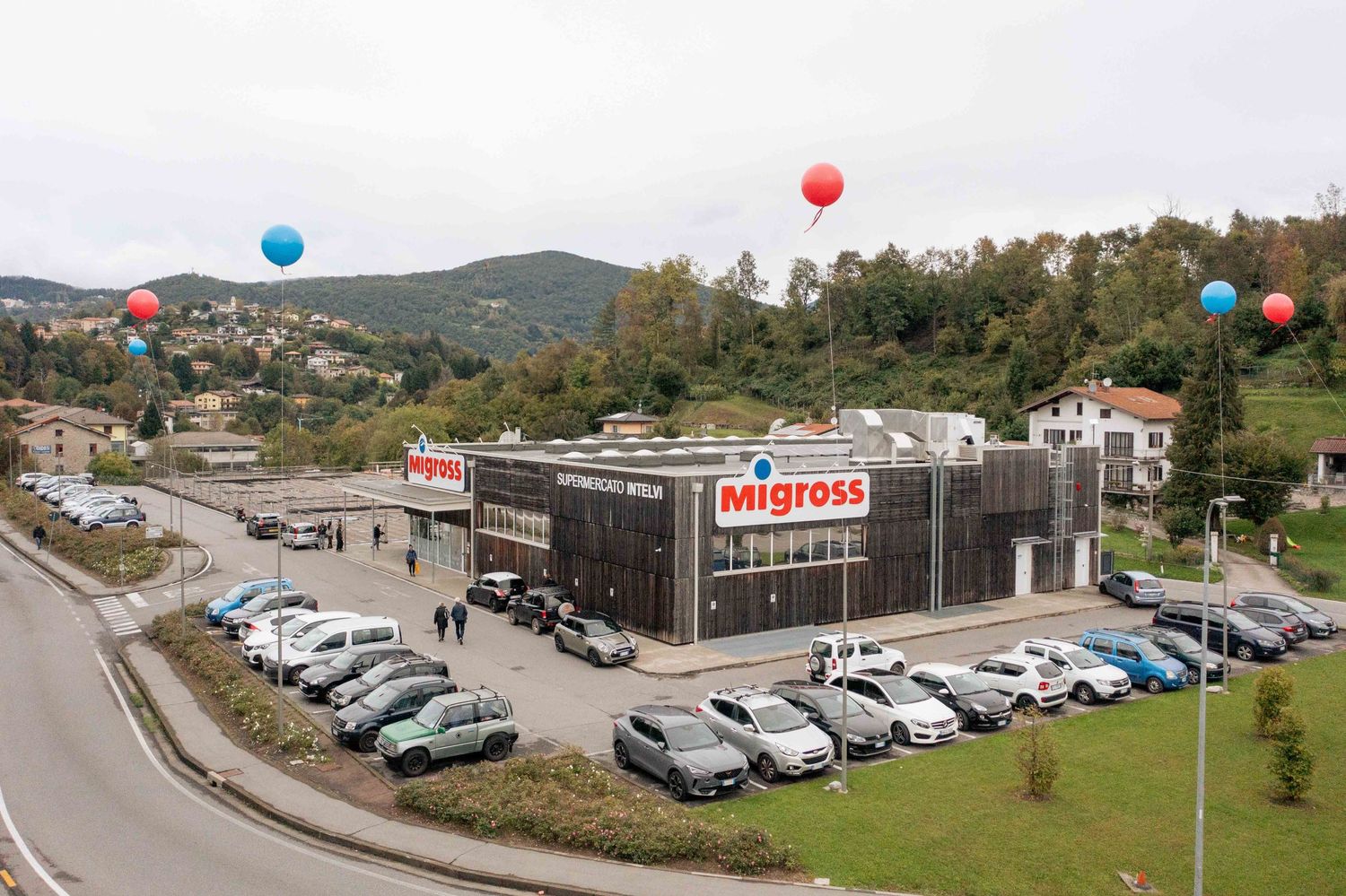 Aerial view of a commercial property with parking lots and buildings surrounded by trees and mountains.