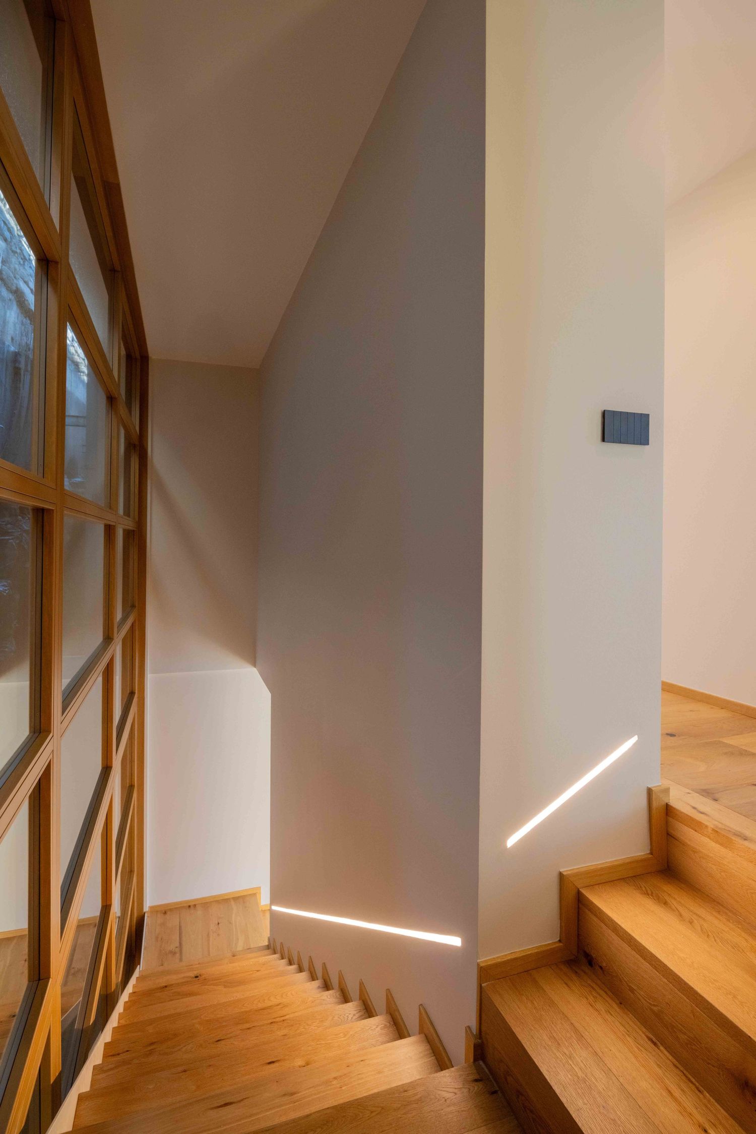 Contemporary staircase with wooden steps and white walls featuring angular window design.