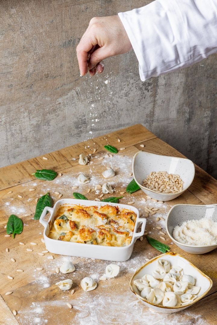 Step by step process of preparing a baked pasta dish with cheese and fresh basil leaves on a wooden cutting board.