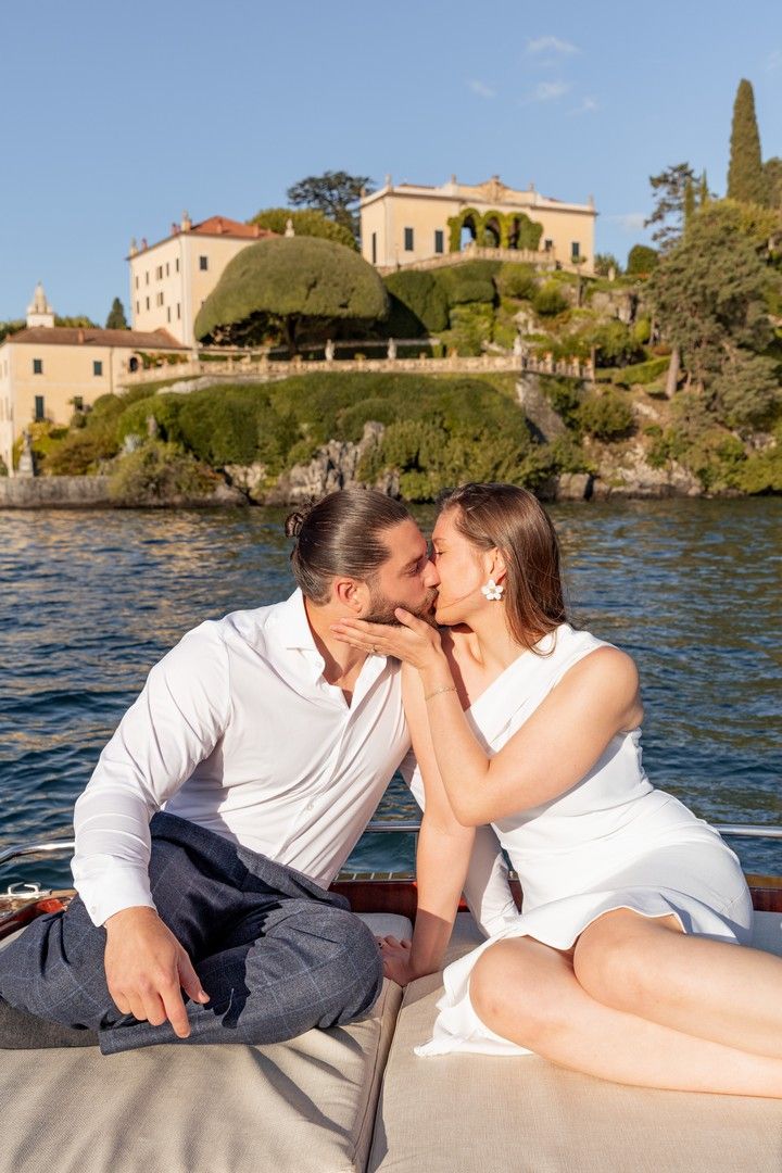 Couple enjoying an intimate moment on a wooden boat with Mediterranean villas in the background.