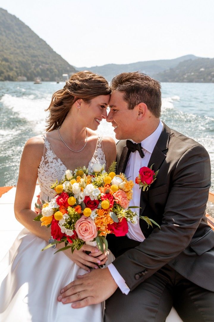 A couple poses with vibrant yellow and orange wedding bouquet against ocean backdrop.