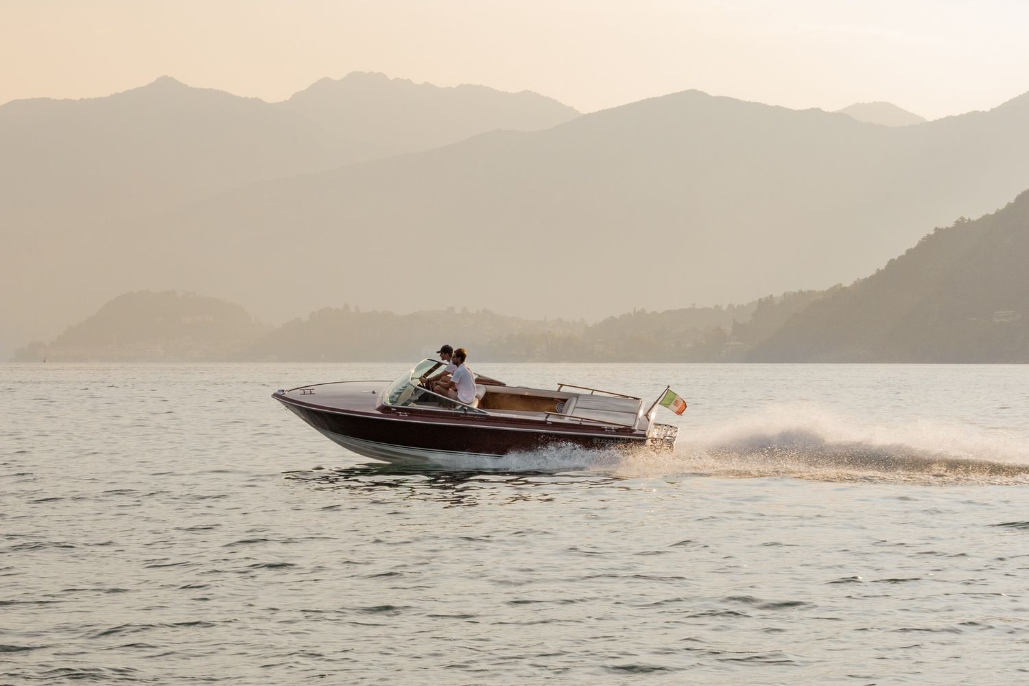 Classic wooden boats speed across Lake Como with mountains and villas in the background.