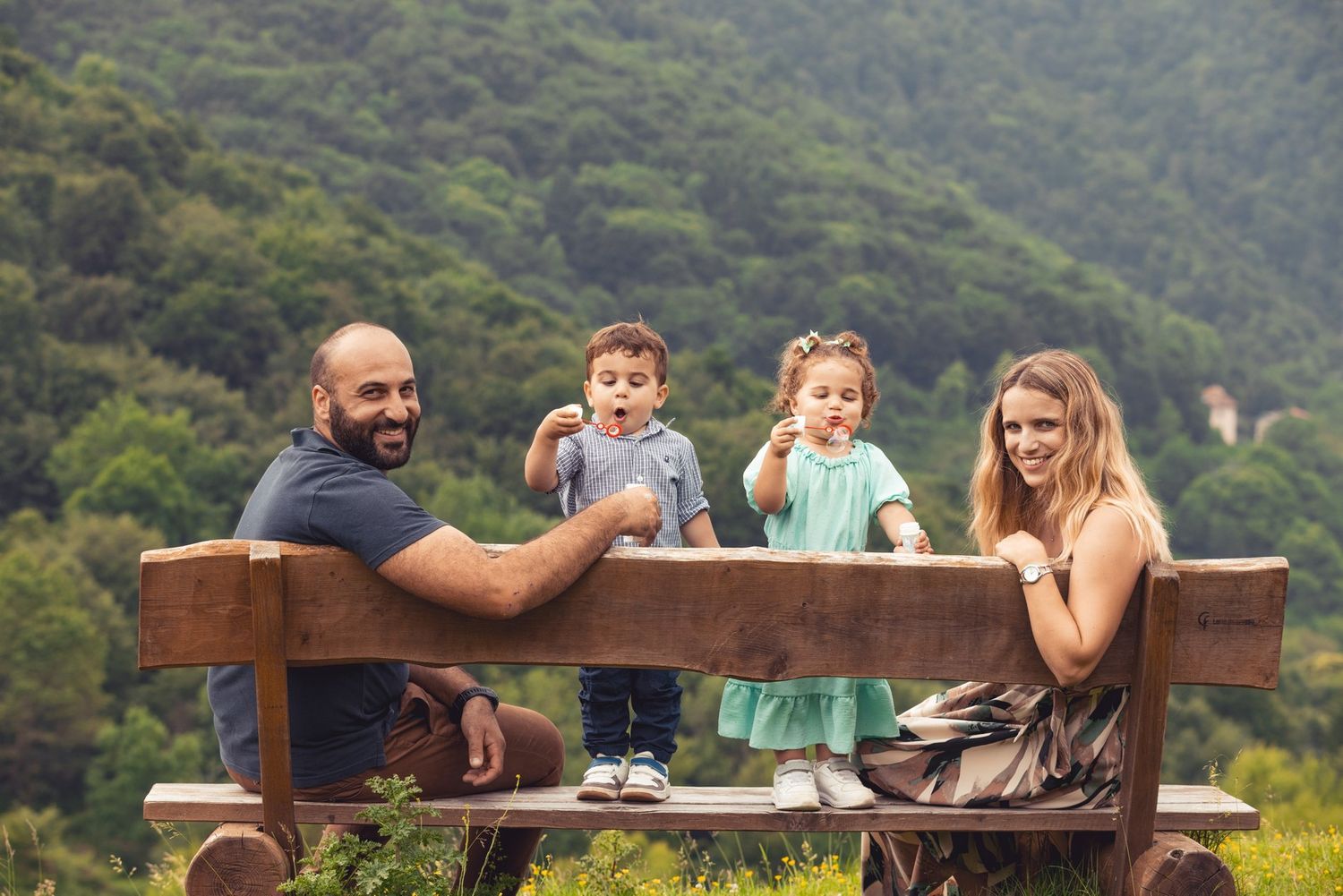 Group relaxing on a wooden bench overlooking mountain scenery on a sunny day.